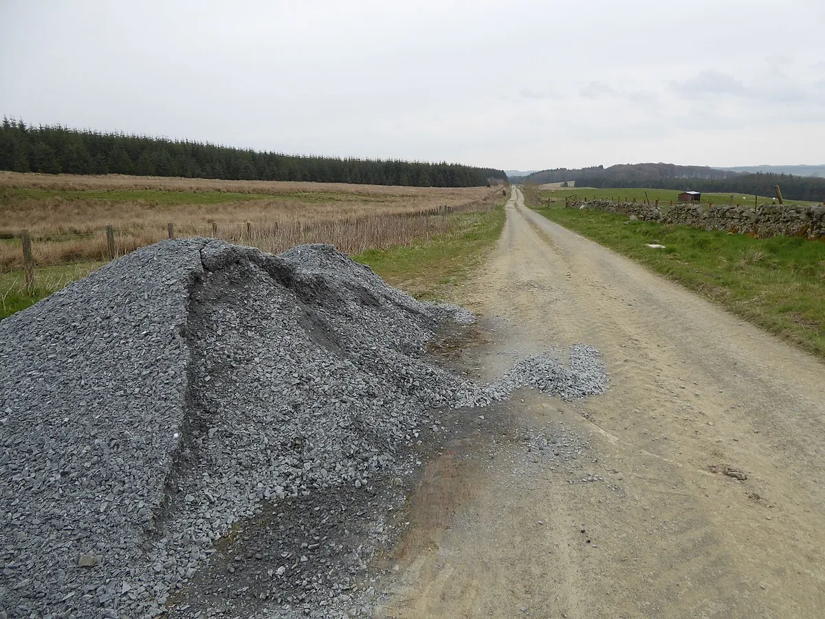 Pile of crushed stone beside a rural gravel lane, ready to fill potholes
